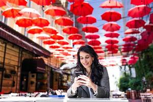 Charming woman with beautiful smile reading good news on mobile phone during rest in coffee shop, happy Caucasian female watching her photo on cell telephone while relaxing in cafe during free time