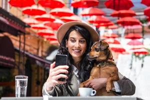 Young woman with her dog in pet friendly cafeteria. Girl drinking coffe at local coffee shop with her pet dog taking a selfie with mobile phone photo