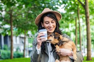 happy hipster woman playing with her dog and drinking coffee. stylish girl with funny dog resting, hugging and having fun in sun, cute moments. space for text photo