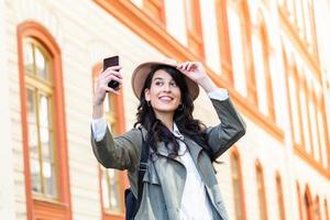 Tourist posing for a selfie in a street. Vlogger recording content for her travel vlog. Cute young smiling girl is making selfie on a camera while walking outdoors. photo