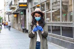 Young woman on the street wearing face protective mask to prevent Coronavirus COVID-19 and anti-smog and using smartphone photo