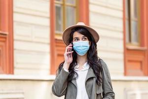 Portrait of young woman on the street wearing face protective mask to prevent Coronavirus and anti-smog and using smartphone photo