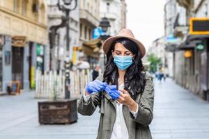 Portrait of young woman on the street wearing face protective mask to prevent Coronavirus and anti-smog and using smartphone taking off her gloves photo