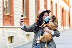 mujer durante el aislamiento pandémico caminando con su perro y usando el teléfono móvil para hacer un selfie. chica elegante con un perro divertido descansando, abrazándose y divirtiéndose, lindos momentos. foto