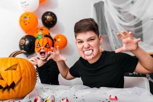 Scary boy with vampire fangs looking at the camera on thehalloween party. Jack O' Lantern Halloween pumpkin on the table photo