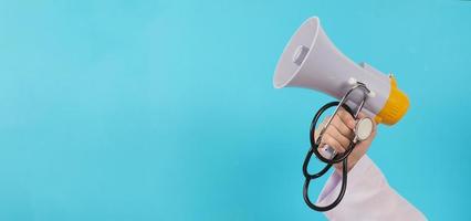 The doctor's hand is holding a megaphone and stethoscope on blue background. photo