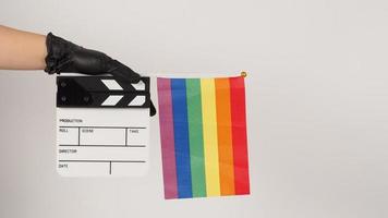 Hands are holding a movie slate or clapper board and a rainbow flag. Hands are wearing black latex gloves photo