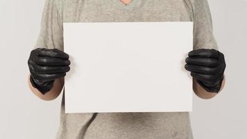 las manos sostienen el papel a4 y usan guantes de látex con una camiseta gris sobre fondo blanco. foto