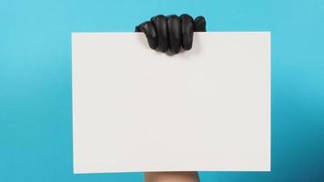 Hand is holding the A4 paper and wear black latex glove on blue background. photo