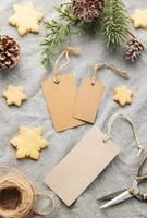 etiquetas de regalo en blanco con rama de pino y galletas de Navidad sobre fondo textil. el concepto de preparación para las vacaciones de navidad foto