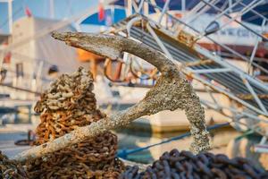 View of the old rusty anchor with a chain in the port of the city. Anchor of an old ship on the pier, selective focus, background or screen about holidays at sea and travel photo