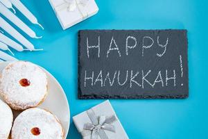 Happy Hanukkah. Jewish dessert sufganiyot donuts on blue background. Symbol of religious Judaism holiday. Inscription on chalk board.