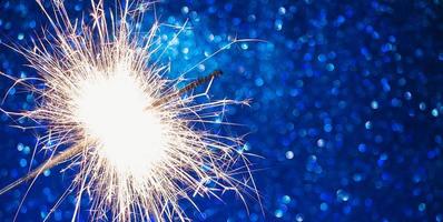 bengala brillante sobre fondo azul. celebrando año nuevo y navidad. chispas brillantes de fuego y bokeh. foto