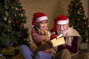 pareja caucásica mayor celebrando la navidad juntos en felicidad y emoción en casa con sombrero de santa y árbol de navidad foto