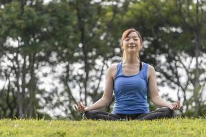 joven asiática con traje de yoga practicando relajadamente la meditación en el bosque para alcanzar la felicidad de la sabiduría de la paz interior para el ejercicio respiratorio, el concepto sano de la mente y el alma foto