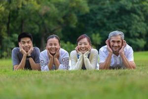 Portrait of group of Asian family with father, mother, son and daughter lying down together on the grass lawn at the public park during weekend activity for recreation and wellbeing concept photo