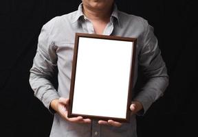 A blank diploma or a mockup certificate in the hand of a man employee wearing shirt on black background. The vertical picture frame is empty and the copy space. photo