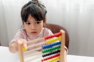 A young cute Asian girl is using the abacus with colored beads to learn how to count at home photo