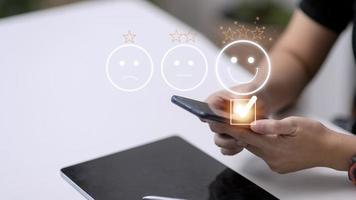 Customer service evaluation concept. using a smartphone is pressing face emoticon smiling in satisfaction on virtual touch screen. photo