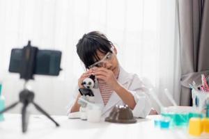 Asian school girl making easy chemistry experiments and recording a video for his followers, Young blogger kid posing in front of camera for vlog, Children make vlog for social media channel concept. photo