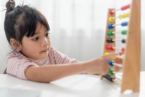 A young cute Asian girl is using the abacus with colored beads to learn how to count at home photo