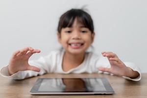linda niña asiática tocando la pantalla de la tableta digital en la mesa foto