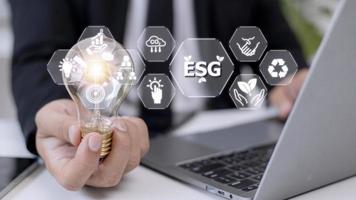 Businessman hand holding light bulb with esg icon on virtual screen, ESG Environmental, social and corporate governance concept photo