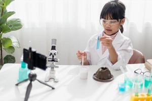 Asian school girl making easy chemistry experiments and recording a video for his followers, Young blogger kid posing in front of camera for vlog, Children make vlog for social media channel concept. photo
