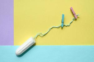 Tampon with two clothespins lie on texture background of fashion pastel violet, yellow and blue colors paper in minimal concept photo