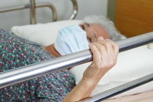 Asian elder senior woman patient holding bed rail while lie down with hope waiting her family in hospital. photo
