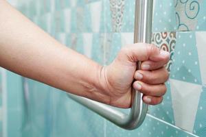 Asian woman patient use toilet support rail in bathroom, handrail safety grab bar, security in nursing hospital. photo