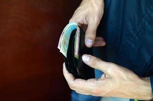 Man holds in hands black leather wallet with ukrainian money or thief who stole wallet full of money photo