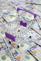 Empty small shopping cart lies on a many dollar bills photo