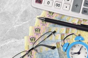 1 billete de hryvnia ucraniano y calculadora con gafas y bolígrafo. préstamo comercial o concepto de temporada de pago de impuestos. hora de pagar impuestos foto
