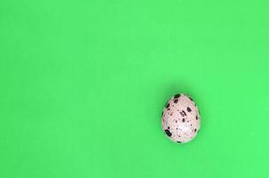 One quail egg on a light green surface, top view, empty place fo photo