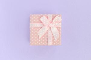 Small pink gift box with ribbon lies on a violet background. Minimalism flat lay top view photo