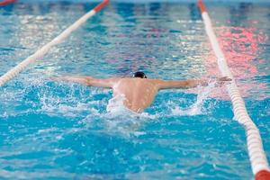 un nadador agita sus brazos mientras realiza una mariposa en una sesión de entrenamiento en la piscina, enfoque borroso foto