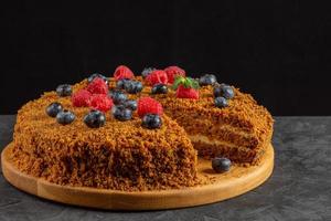 carrot cake decorated with blueberries and raspberries on a dark background photo