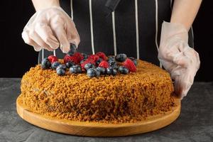 A female chef decorates a homemade carrot cake with fresh berries on a dark background photo