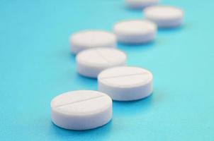 A few white tablets lie on a bright blue background surface. Background image on medical and pharmaceutical topics photo