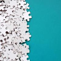 A pile of uncombed elements of a white jigsaw puzzle lies on the background of a blue surface. Texture photo with copy space for text