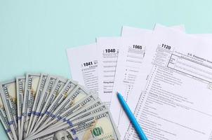 Tax forms lies near hundred dollar bills and blue pen on a light blue background. Income tax return photo