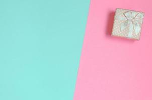 una pequeña caja de regalo rosa se encuentra en el fondo de textura de papel de colores azul pastel y rosa de moda en un concepto mínimo foto