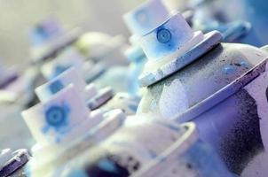 A lot of dirty and used aerosol cans of bright blue paint. Macro photograph with shallow depth of field. Selective focus on the spray nozzle photo