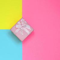 Small pink gift box lie on texture background of fashion pastel blue, yellow and pink colors paper in minimal concept photo