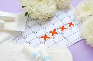 almohadillas menstruales y tampones en el calendario del período de menstruación con flores blancas sobre fondo lila foto