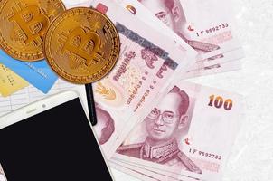 Billetes de 100 baht tailandeses y bitcoins dorados con smartphone y tarjetas de crédito. concepto de inversión en criptomonedas. criptominería o comercio foto