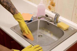 Person or householder cleaning the kitchen sink with sponge in close up view photo