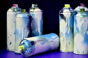 Still life with a large number of used colorful spray cans of aerosol paint lying on the treated wooden surface in the artist's graffiti workshop. Dirty and stained cans for spray art photo