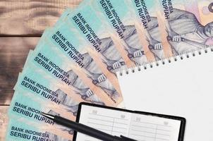 Ventilador de billetes de 1000 rupias indonesias y bloc de notas con libreta de contactos y bolígrafo negro. concepto de planificación financiera y estrategia empresarial foto